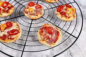 Small mini pizzas topped with cheese, tomato, yellow and red bell peppers and salami sausage on round black grid