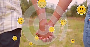 Multiple smiling face emoji floating against mid section of couple holding hands