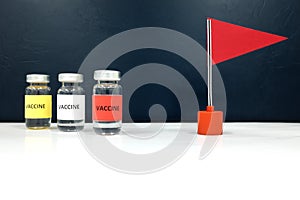 Multiple vaccine vials and a red flag. Coronavirus covid-19 vaccine candidate development race and competition winner concept.
