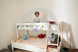 Multiracial boy looking at the camera with happy smile while standing at the second tier of his bed