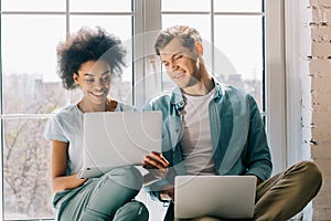 Multiracial boyfriend and girlfriend using laptops while sitting