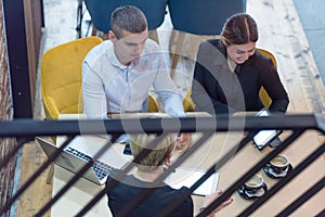 Multiracial business people working connected with technological devices at the bar. Group of three young creative coworkers