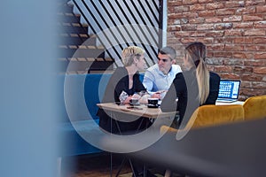 Multiracial business people working connected with technological devices at the bar. Group of three young creative coworkers