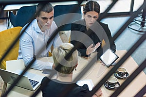 Multiracial business people working connected with technological devices at the bar. Group of three young creative coworkers