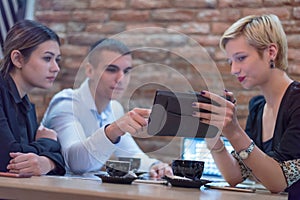 Multiracial business people working connected with technological devices at the bar. Group of three young creative coworkers