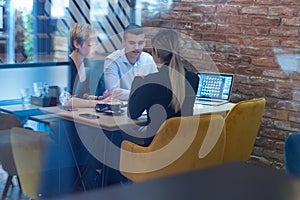 Multiracial business people working connected with technological devices at the bar. Group of three young creative coworkers