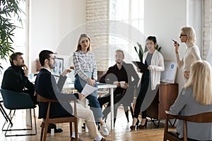 Multiracial businesspeople listening to confident young female speaker.