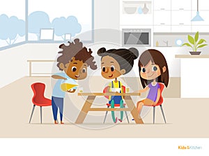 Multiracial children preparing lunch by themselves and eating. Two girls sitting at table and boy pouring orange juice into glass.