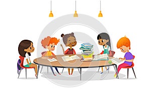 Multiracial children sitting around round table with pile of books on it and listening to girl reading aloud. School photo