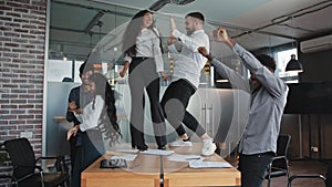 Multiracial colleagues dancing in office celebrating victory company success good deal man and woman moving on table in
