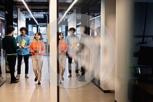 Multiracial colleagues discussing while businesswoman walking with tablet pc in corridor at office