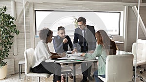 Multiracial colleagues gather in office boardroom discussing paperwork