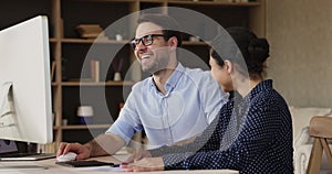 Multiracial colleagues talking funny jokes laughing seated at workplace