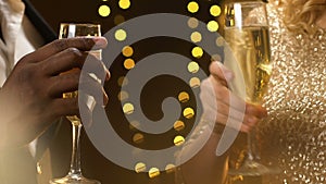 Multiracial couple clinking champagne at new year party, lights glowing, closeup