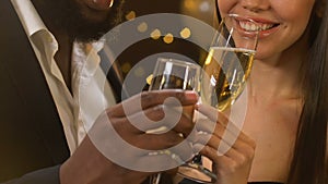 Multiracial couple clinking glasses with champagne and chatting at party, flirt