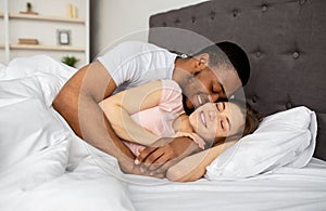 Multiracial couple cuddling in bed at home, hugging each other, having intimate foreplay after waking up in morning