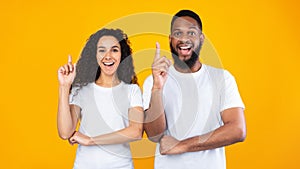 Multiracial Couple Pointing Fingers Up Having Idea Over Yellow Background