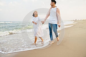 Multiracial couple smiling and holding hands while walking on beach