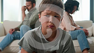 Multiracial diverse family annoyed married couple after quarrel sit separated on home sofa upset sad little boy kid son