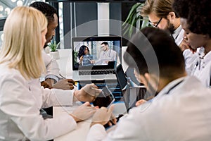 Multiracial doctors having a video conference at light office with two African and Caucasian doctors holding CT, sitting