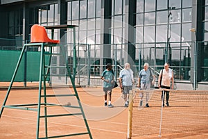 multiracial elderly friends with tennis equipment walking