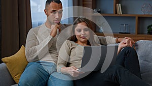 Multiracial ethnic couple homeowners shopping online use laptop hug on sofa at home diverse woman wife and man husband