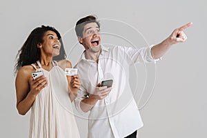 Multiracial excited man and woman posing with cellphones and credit card