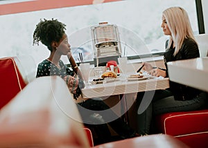 Multiracial female friends eating fast food at a table in the di