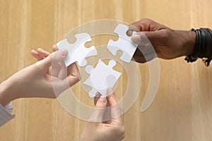 Multiracial female male hands holding puzzle pieces above table