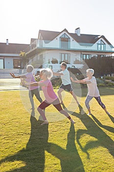 Multiracial female and male seniors exercising on grassy land in yard against retirement home