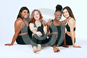 Multiracial females with different size and ethnicity stand together and smile.