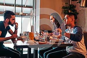 Multiracial friends eat breakfast in cafe. Young men chat while having tasty food and drinks. Guys hangout together