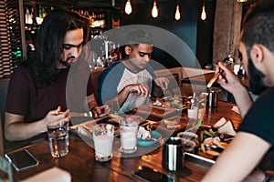 Multiracial friends eating breakfast in cafe. Young men chat while having tasty food and drinks. Guys hangout together