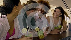 Multiracial friends enjoying cocktails at beach bar, laughing and having fun. 4k video.