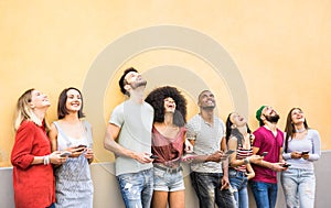 Multiracial friends having fun using smartphone at wall on university college break - Young people addicted by mobile smart phones