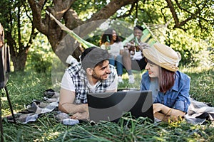 Multiracial friends with laptop relaxing at garden