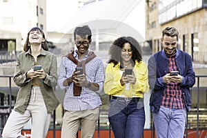 Multiracial friends laughing using smartphone in the university district of the city - Young people addicted by mobile smart