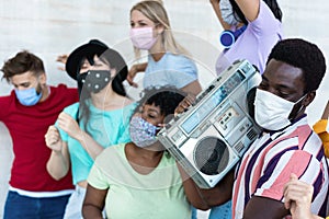 Multiracial friends with masks dancing and listening music with boombox stereo outdoor - Main focus on black man
