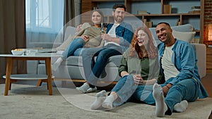 Multiracial friends men women watching television at home hispanic couple relax on couch african american caucasian