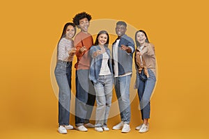 Multiracial friends pointing and laughing on orange background
