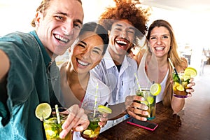 Multiracial friends taking selfie at beach bar looking at camera having cocktails. Friends having fun at summertime