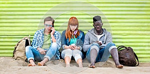 Multiracial friends using mobile smart phone at beach on relax moment - Young bored people addicted by smartphone