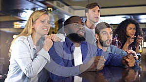 Multiracial friends watching sports in bar, upset about losing game, defeat