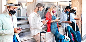 Multiracial friends wearing face mask using mobile smart phones - Young millenial checking online reservations at train station photo