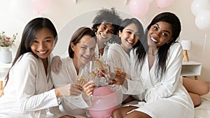 Multiracial girls in bathrobes holding champagne glasses celebrating bachelorette party