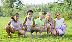 Multiracial group of cheerful preteen friends posing on green lawn