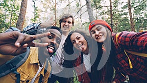 Multiracial group of friends travelers is taking selfie in wood looking at camera, posing with funny faces and gestures