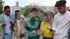 Multiracial group of friends using mobile phone while walking together in city