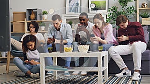 Multiracial group of friends using smartphones touching screen on sofa at home