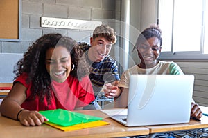 Multiracial group of high school students laughing together in class using laptop to do homework together.
